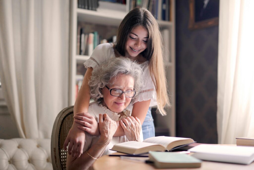 Young woman hugging grandmother reading book.